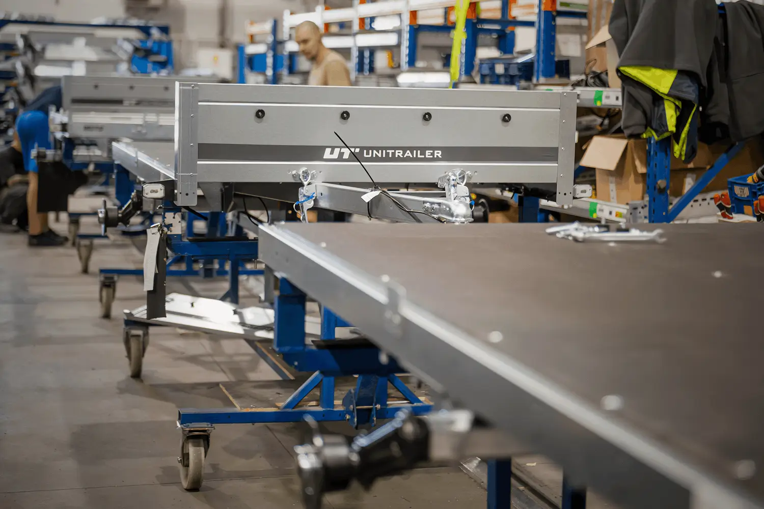 Overzicht van een productiefaciliteit waar metalen onderdelen en frames van aanhangwagens worden geassembleerd en op transportwagens worden geplaatst.