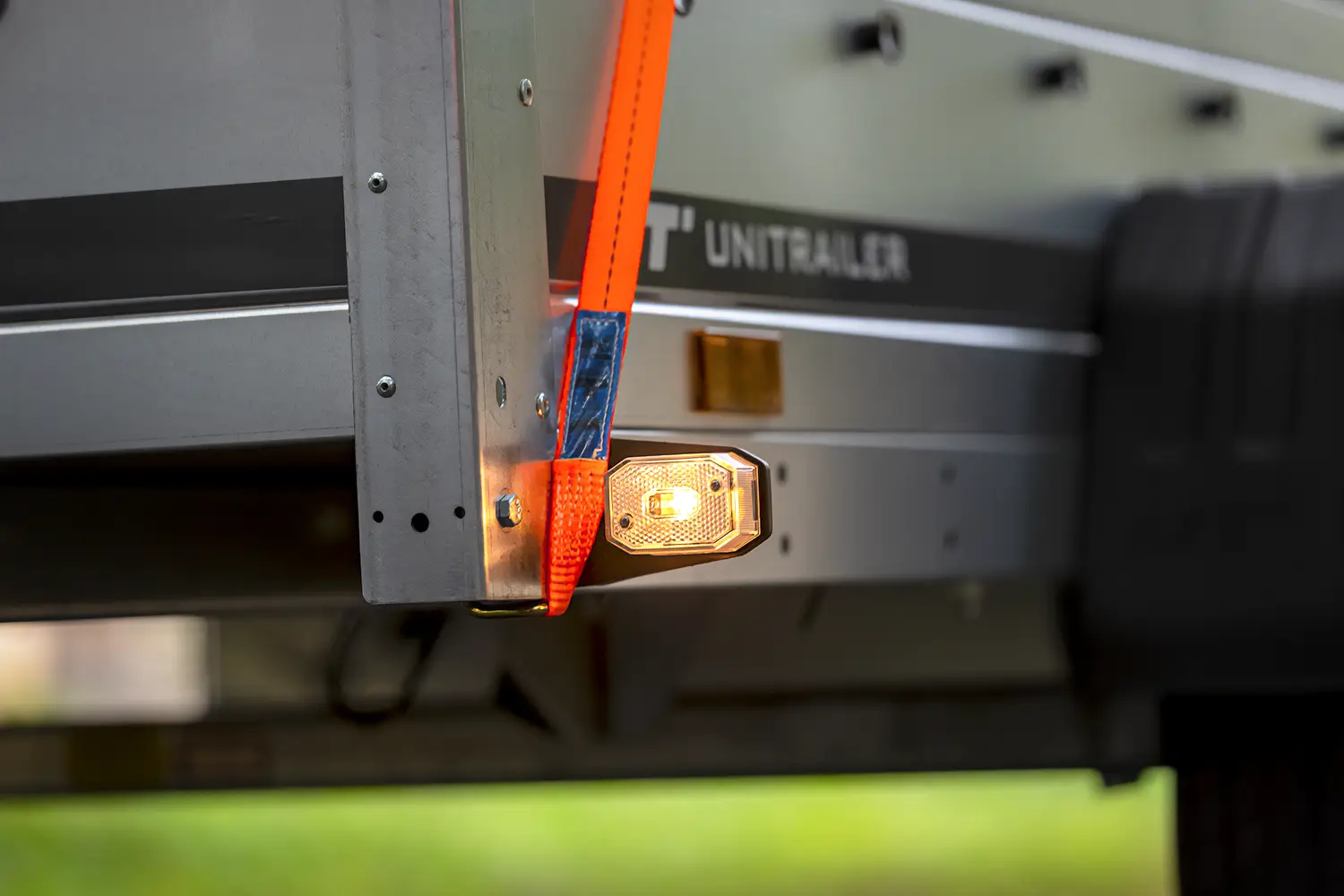 Close-up van een oranje spanband die de lading vastzet en een ingeschakeld markeringslicht op het zijbord van de aanhangwagen.